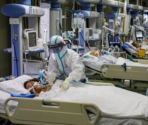 A frontline health worker in full PPE tends to a patient in a COVID-19 intensive care unit